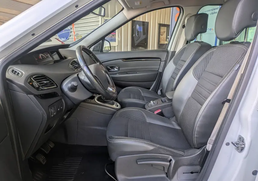 Vue intérieure côté conducteur du Renault Scenic IV blanc, mettant en valeur les sièges noirs bi-matière et le tableau de bord épuré.