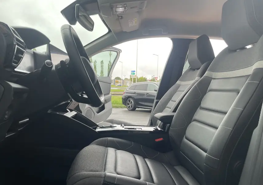 Vue intérieure côté conducteur de la Citroën C4 blanche 2022, sièges tissu gris noir et volant multifonction.