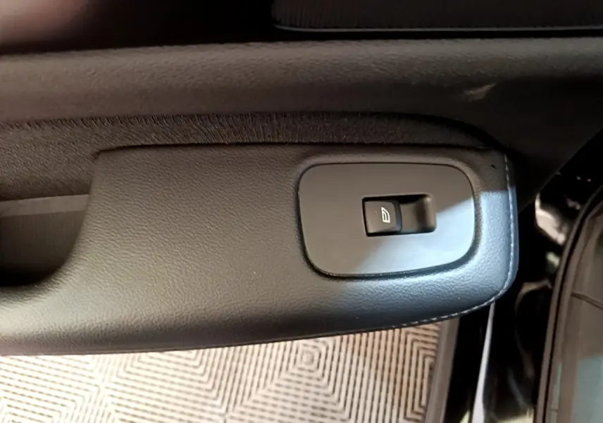 Gros plan sur le bouton de commande de la vitre électrique côté porte intérieure d’une Volvo V60 noire.