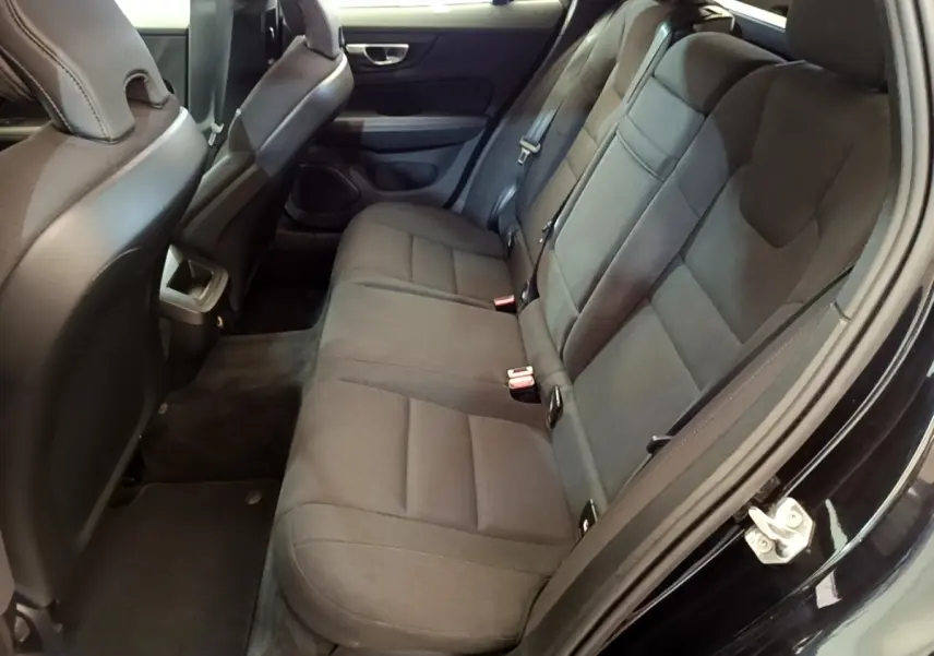 Vue intérieure côté droit montrant la banquette arrière noire de la Volvo V60 avec sièges en tissu et ceintures de sécurité.