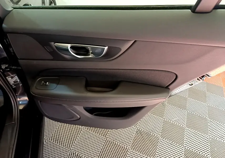 Vue intérieure côté gauche de la porte avant noire d'une Volvo V60 2020 avec poignée chrome et commandes de vitre.