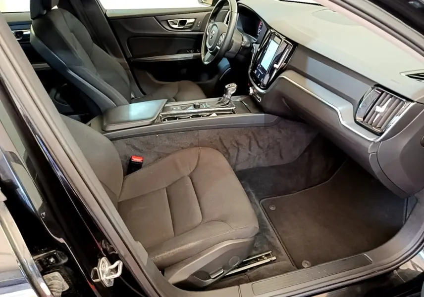 Intérieur avant droit d’une Volvo V60 noire 2020, avec tableau de bord moderne et sièges tissu gris foncé.