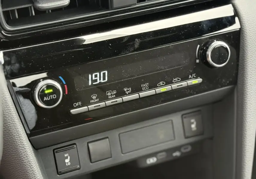 Gros plan sur la console centrale noire du Toyota Yaris Cross 1.5 Hybrid 116 Design, affichant la climatisation à 19°C.