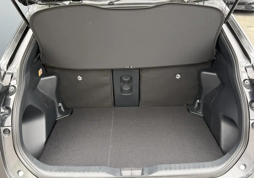Coffre ouvert vu de l'arrière d'une Toyota Yaris Cross gris Atlas, montrant un plancher plat et un cache-bagages.