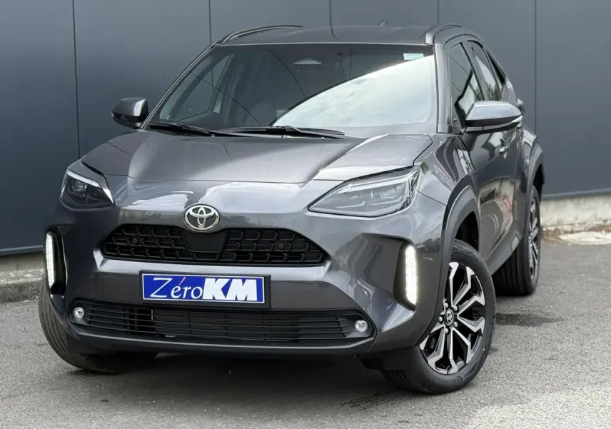 Toyota Yaris Cross gris Atlas vue 3/4 avant droit, avec feux LED allumés et jantes noires bicolores.