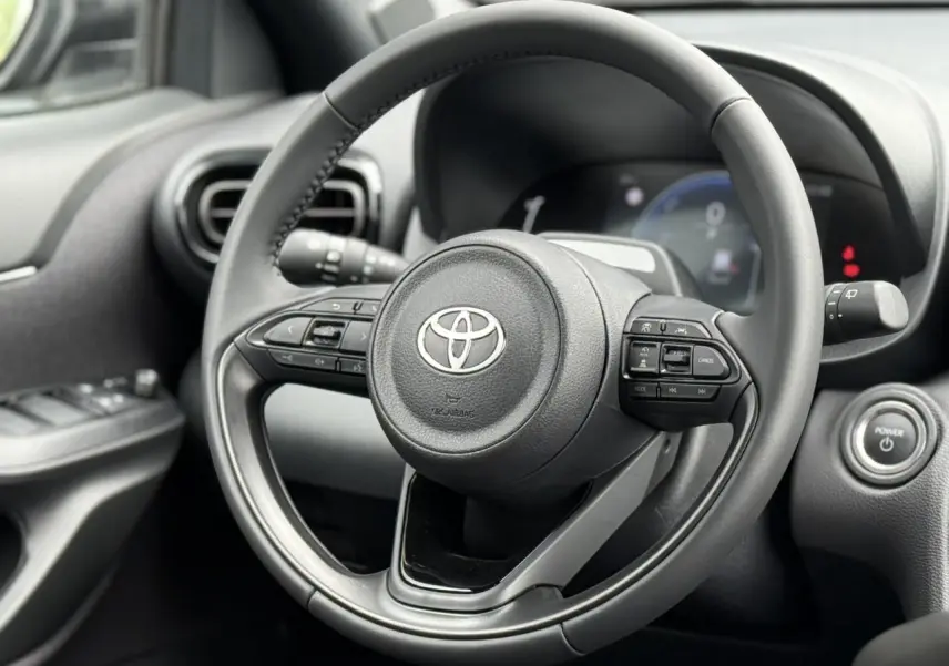 Vue rapprochée du volant cuir noir de la Toyota Yaris Cross 1.5 Hybrid 116 Design avec commandes intégrées.