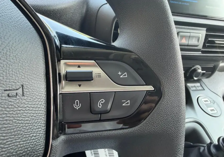 Gros plan sur les commandes du volant cuir noir du Peugeot Partner blanc, avec boutons multifonctions et tableau de bord en arrière-plan.
