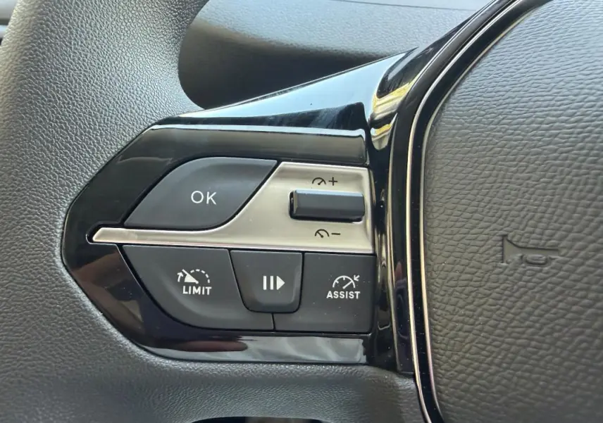 Gros plan sur les commandes à gauche du volant cuir du Peugeot Partner blanc, avec boutons limiteur et assistant de vitesse.