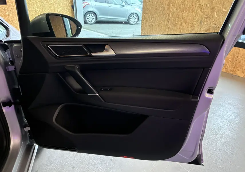 Porte avant gauche ouverte d'une Volkswagen Golf Sportsvan gris, intérieur noir avec poignée argentée et haut-parleur intégré.