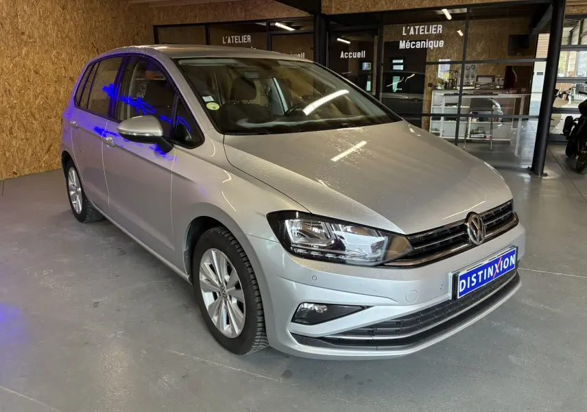 Volkswagen Golf Sportsvan gris vue 3/4 avant droit dans un atelier avec plaque Distinxion visible.