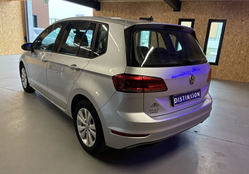 Vue 3/4 arrière droit d'une Volkswagen Golf Sportsvan gris métallisé dans un garage lumineux.