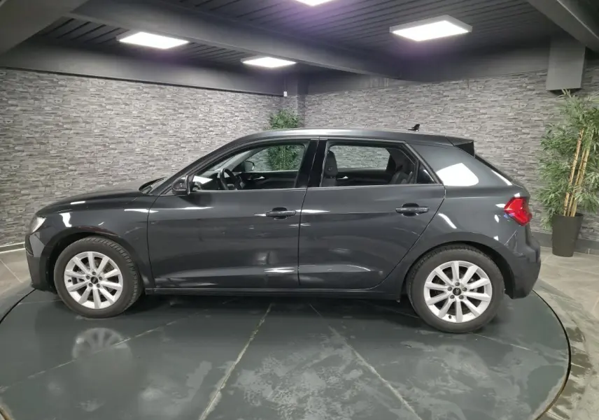 Profil côté gauche d'une Audi A1 Sportback gris Manhattan 2024 avec jantes argentées en intérieur showroom.