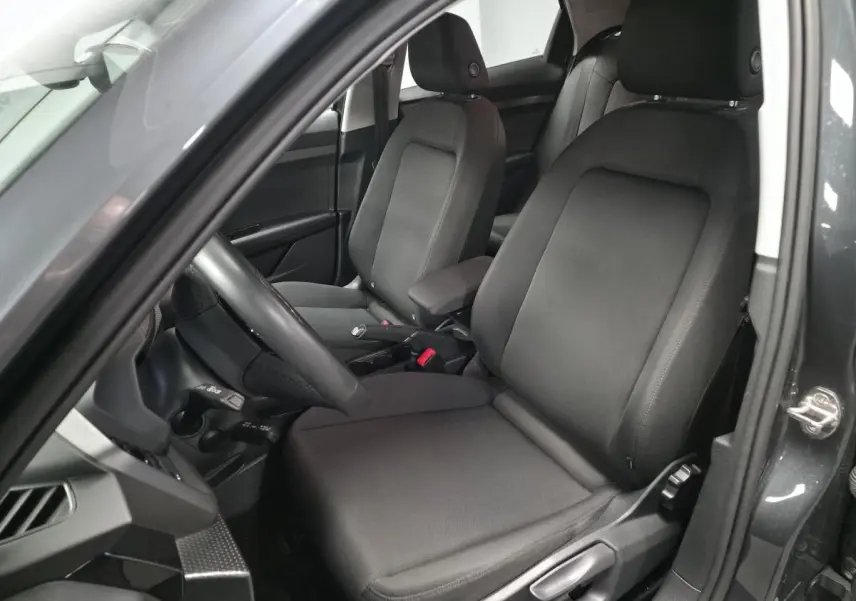 Vue intérieure côté conducteur de l'Audi A1 Sportback 2024 gris Manhattan, sièges sport en tissu Novum et accoudoir central.