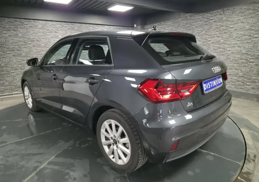 Audi A1 Sportback gris Manhattan vue 3/4 arrière droit avec feux LED et jantes argentées en intérieur showroom.