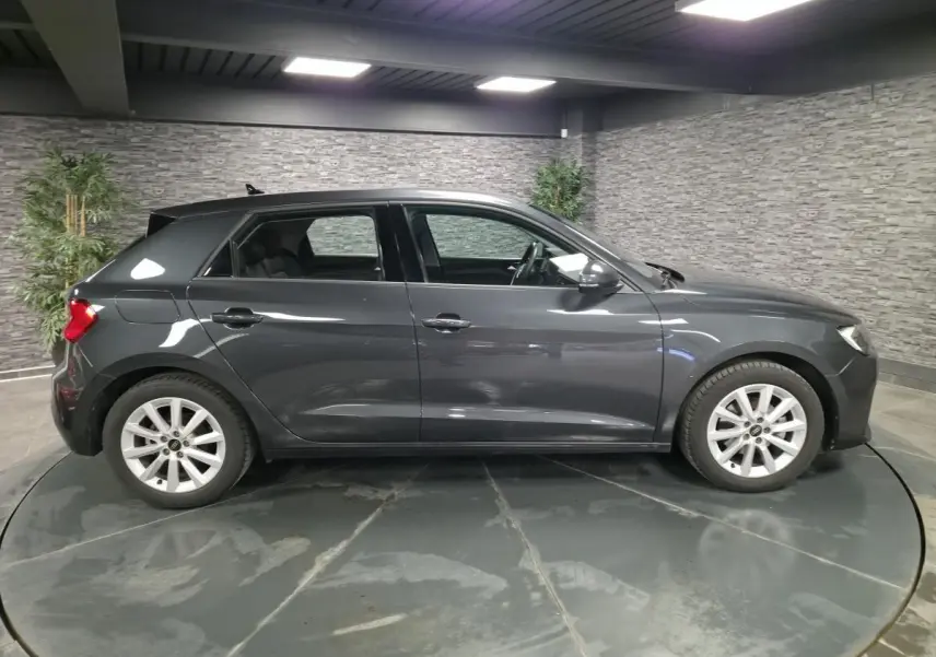 Profil côté gauche d'une Audi A1 Sportback 2024 gris Manhattan avec jantes argentées en intérieur showroom.