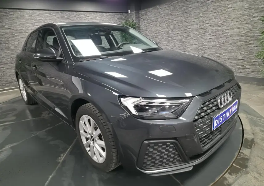 Audi A1 Sportback gris Manhattan vue 3/4 avant droit avec calandre noire et phares LED dans un showroom.