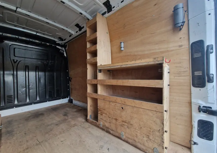 Intérieur du Renault Master blanc vu de l'arrière droit, montrant l'aménagement bois avec étagères et rangements.