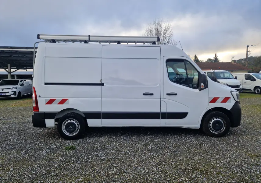 Vue latérale droite d’un utilitaire Renault Master blanc avec galerie de toit et bandes réfléchissantes rouges.