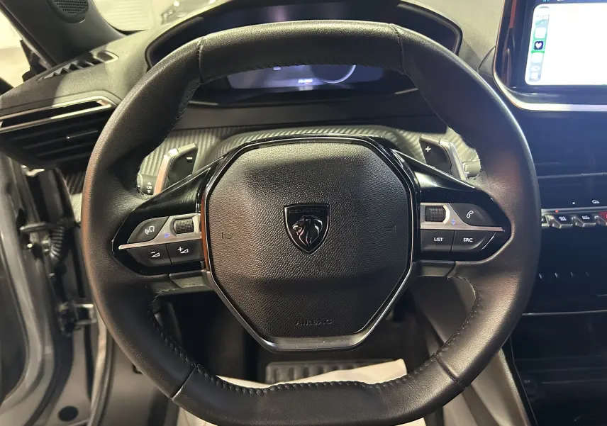 Vue rapprochée du volant cuir noir du Peugeot 2008 Allure Hybrid 145 avec commandes intégrées et tableau de bord numérique.