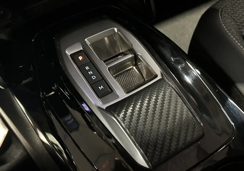 Gros plan sur la console centrale noire brillante avec levier de vitesses automatique et finition carbone du Peugeot 2008 Allure Hybrid 2025.