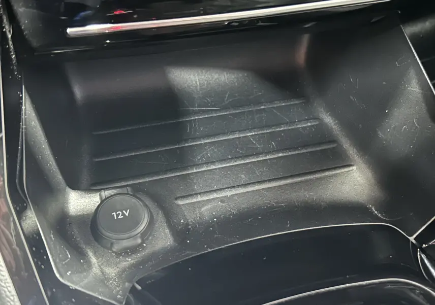 Gros plan sur la prise 12V et le rangement central noir du Peugeot 2008 Allure Hybrid 145 e-DSC6, intérieur moderne.