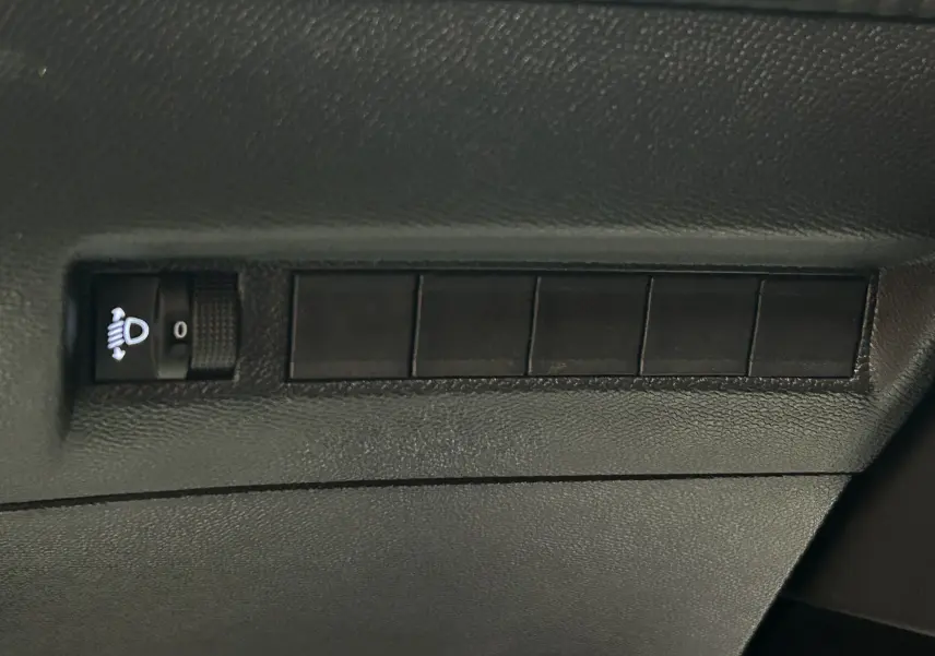 Gros plan sur le bouton de réglage des phares dans l'habitacle d'une Peugeot 2008 Allure Hybrid 2025.