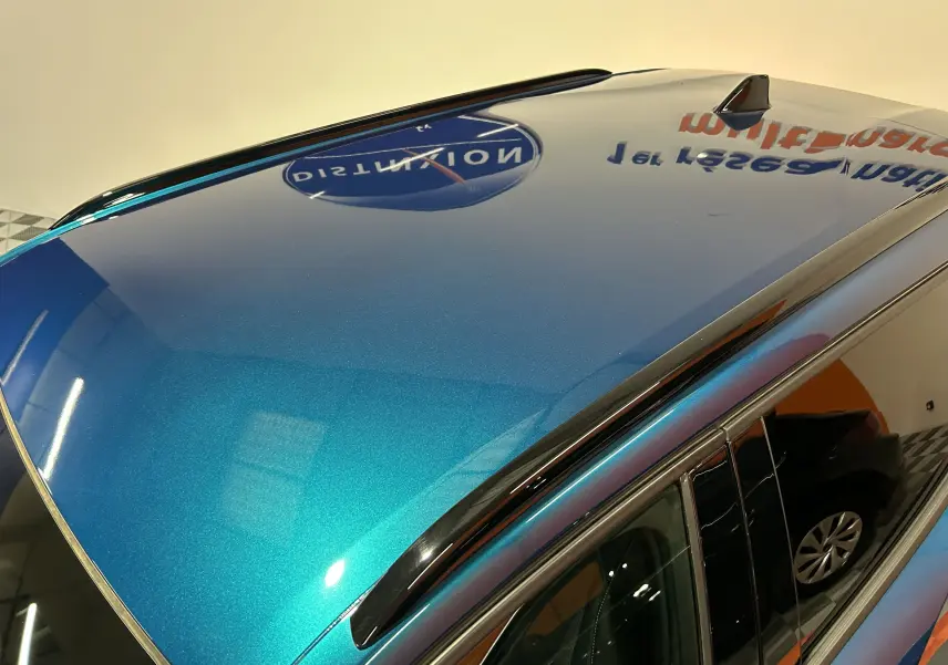 Vue rapprochée du toit bleu obsession métallisé du Peugeot 2008 Allure Hybrid 145 avec antenne requin et barres de toit noires.