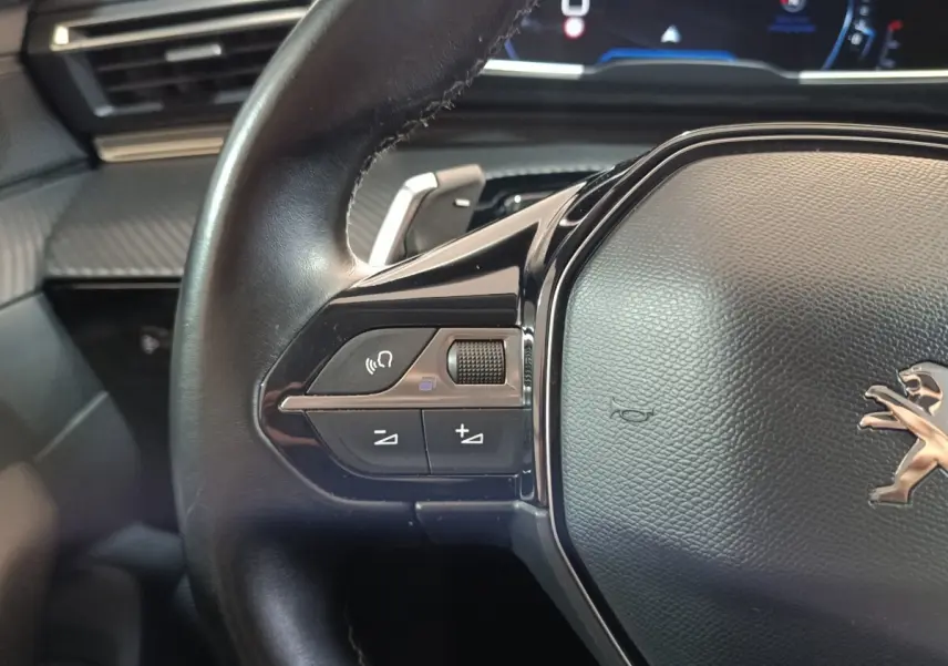 Gros plan sur le volant cuir noir de la Peugeot 508 gris clair, avec commandes vocales et volume intégrées.