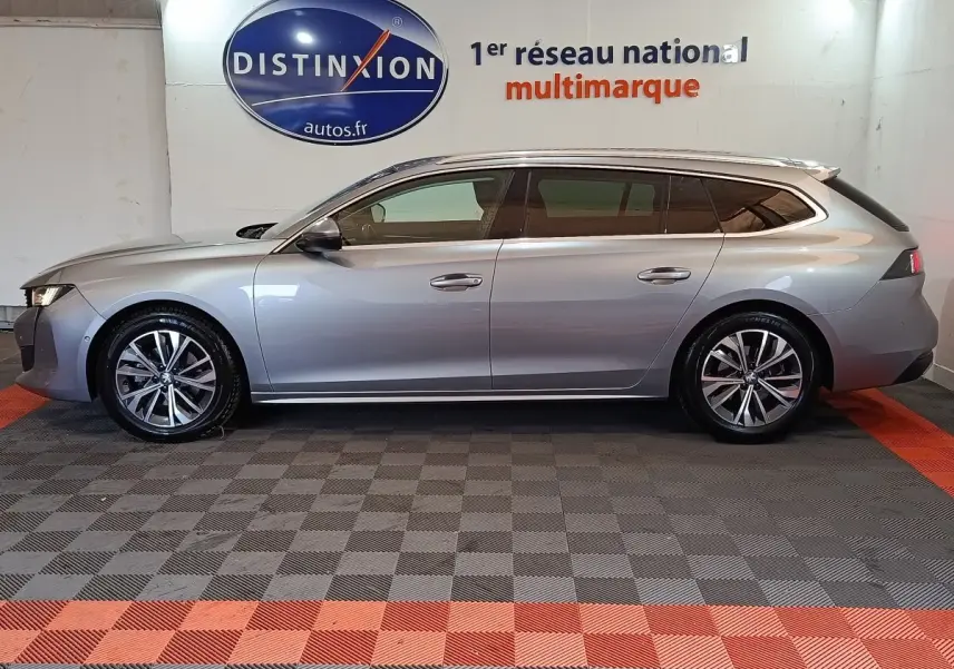 Profil droit d'une Peugeot 508 break gris clair 2020, avec jantes alliage et vitres teintées, en intérieur showroom.