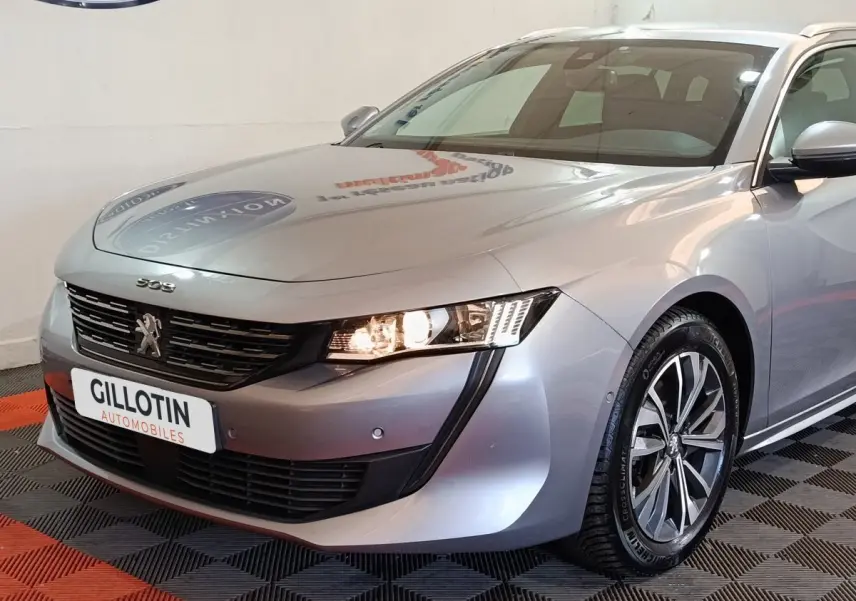 Vue 3/4 avant droit d'une Peugeot 508 gris clair avec phares allumés et jantes alliage distinctives.