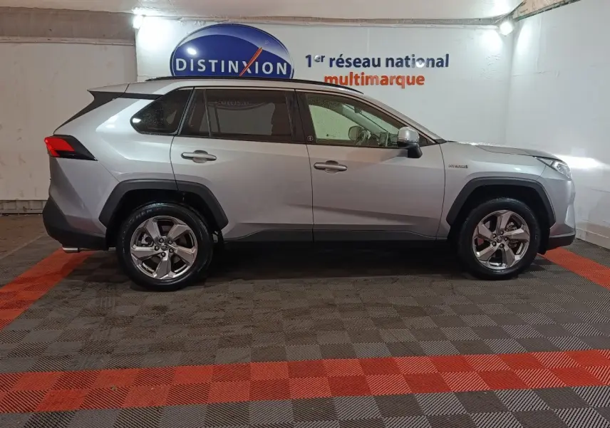 Profil droit du Toyota RAV4 hybride 2WD 2021 gris clair avec jantes alliage et protections noires sur les passages de roues.