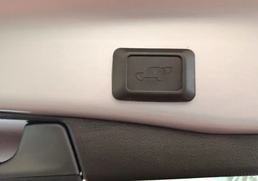 Gros plan sur le bouton d'ouverture électrique du coffre du Toyota RAV4 Hybride 2WD 218ch Dynamic, intérieur noir et beige.