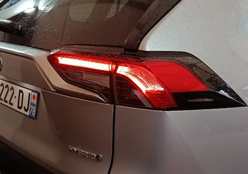Vue arrière droite du Toyota RAV4 hybride gris avec feu arrière allumé et pluie sur la carrosserie.