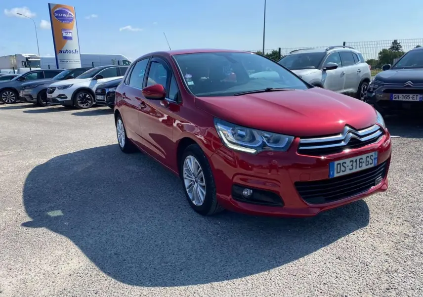 Citroën C4 rouge métallisé vue 3/4 avant droit sur parking avec projecteurs antibrouillard et calandre chromée.