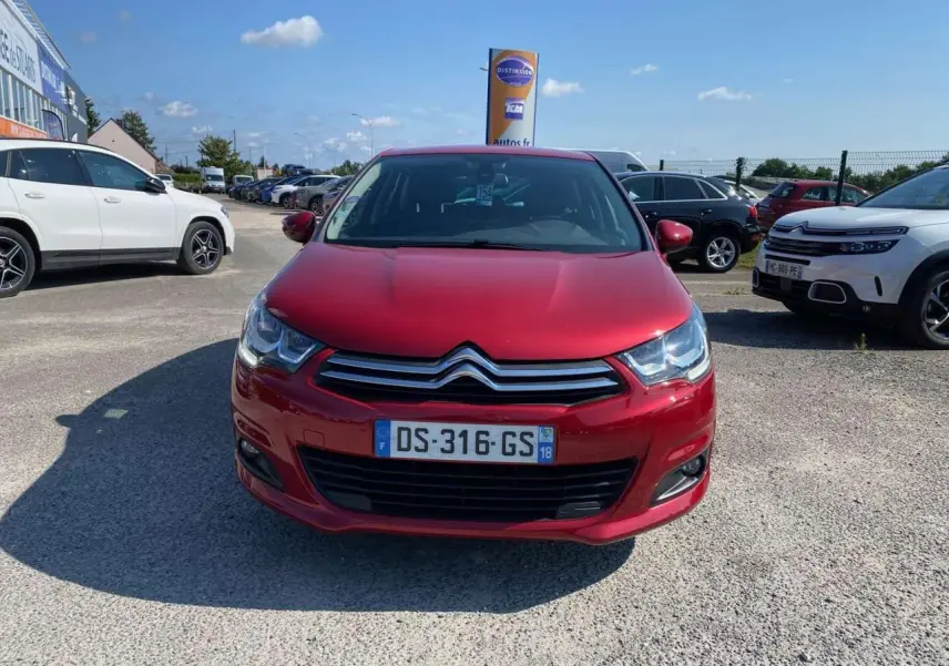 Vue de face d'une Citroën C4 rouge métallisée 2015 avec projecteurs antibrouillard sur un parking extérieur.