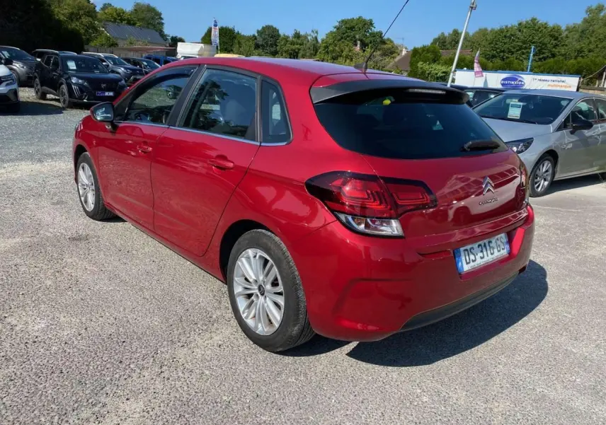 Citroën C4 rouge métallisé vue 3/4 arrière côté gauche, avec feux arrière et lunette teintée visibles.