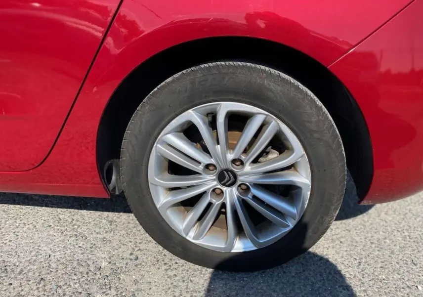 Gros plan sur la roue arrière gauche d'une Citroën C4 rouge métallisée de 2015 avec jante alliage distinctive.