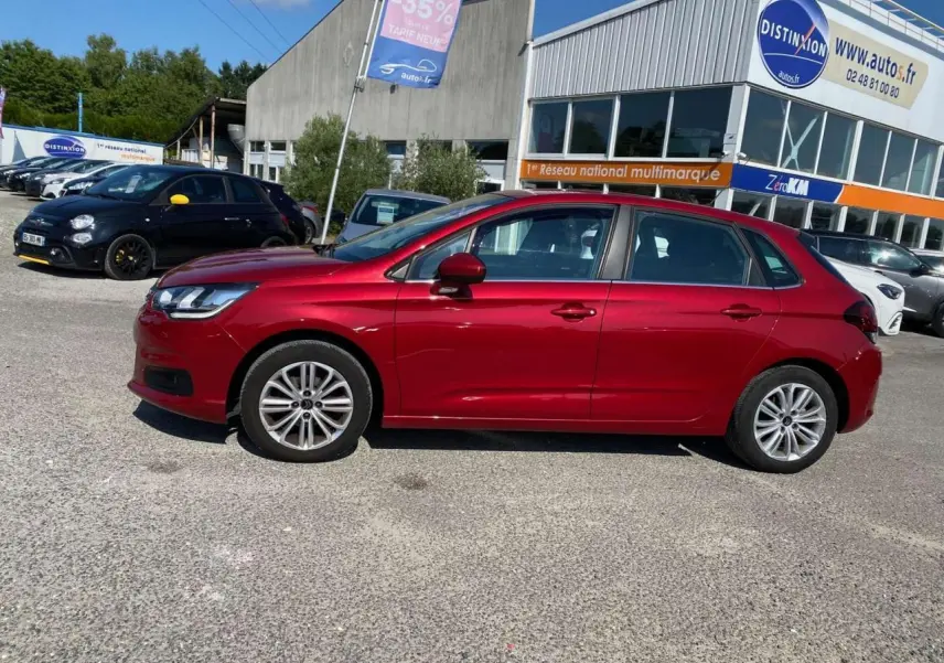 Profil latéral gauche d'une Citroën C4 rouge métallisée de 2015, garée devant un concessionnaire multimarque.