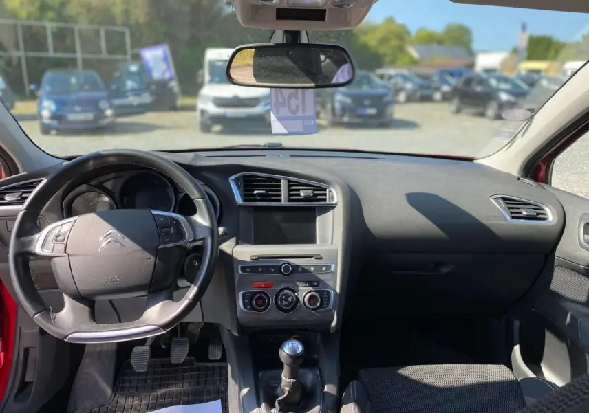 Intérieur avant d'une Citroën C4 rouge 2015, vue du poste de conduite avec tableau de bord et boîte manuelle visible.