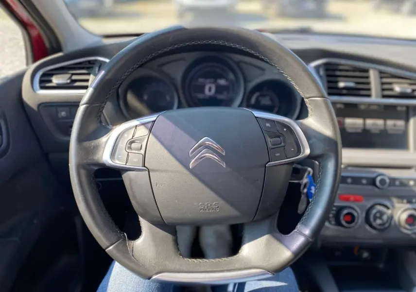 Vue rapprochée du volant cuir noir de la Citroën C4 Millenium 2015 avec commandes intégrées et tableau de bord flou.