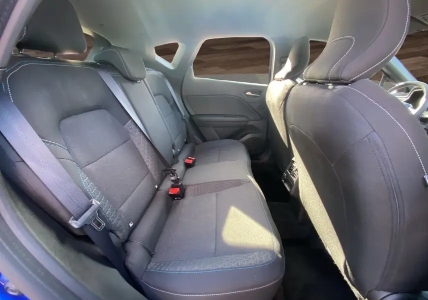 Vue intérieure arrière du Renault Captur 2024, sièges tissu noir avec surpiqûres bleues et ceintures de sécurité visibles.