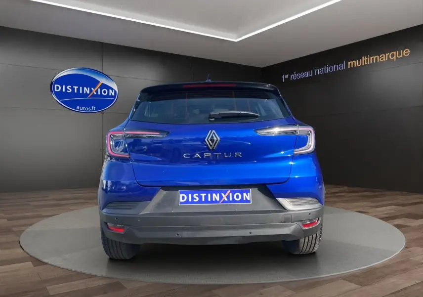 Vue arrière du Renault Captur 2024 bleu Iron avec toit noir et logo distinctif sur fond showroom