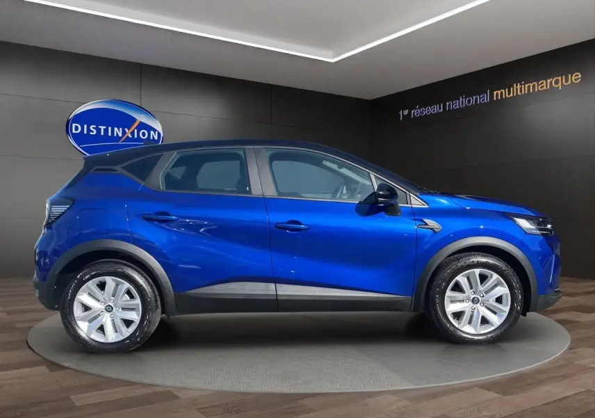 Renault Captur TCE 90 Evolution 2024 en bleu iron avec toit noir, vue profil côté gauche en intérieur showroom.