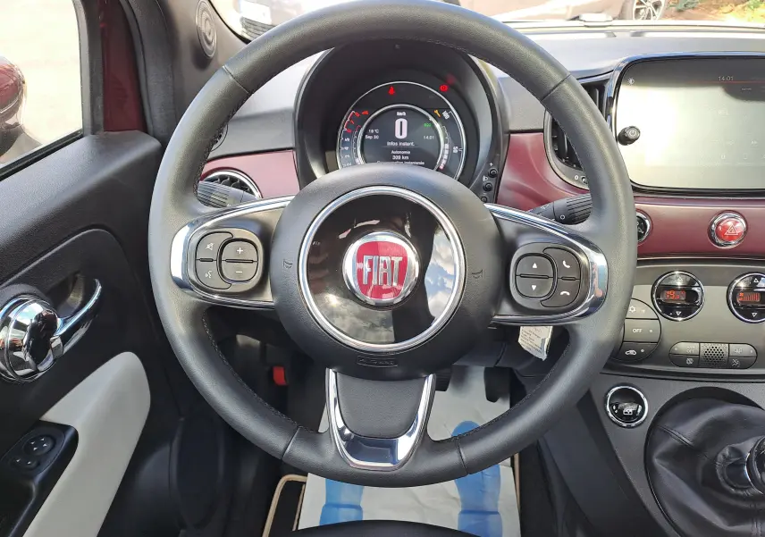 Vue intérieure centrée sur le volant noir et le tableau de bord bordeaux métallisé de la Fiat 500 2020.