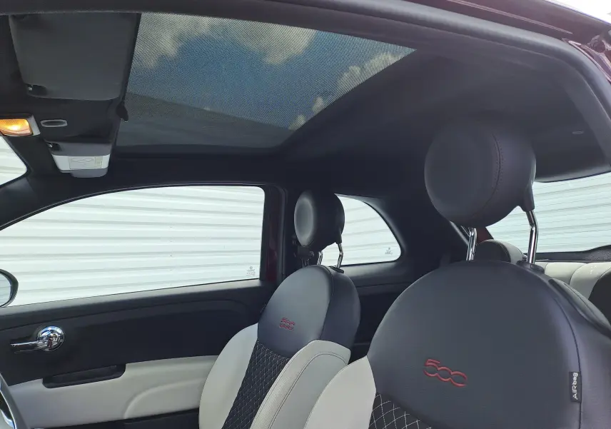 Vue intérieure côté gauche de la Fiat 500 Opera Bordeaux, sièges noirs et blancs avec logo 500 brodé rouge.