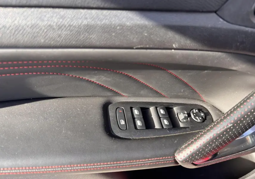 Détail des commandes de lève-vitres sur la porte côté gauche en cuir noir avec surpiqûres rouges de la Peugeot 308 GT Line.