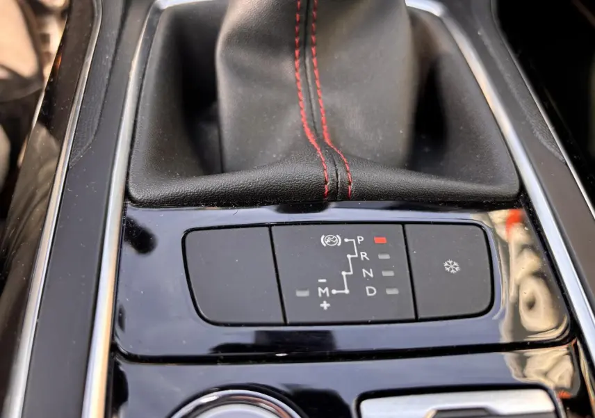 Gros plan sur la console centrale noire brillante de la Peugeot 308 GT Line avec levier de vitesse cuir noir et surpiqûres rouges.