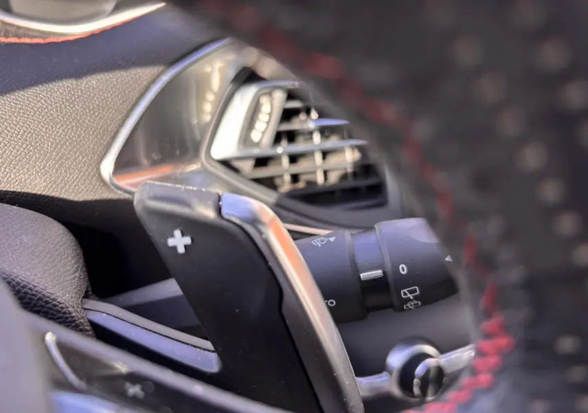 Gros plan sur la palette de changement de vitesse droite et la sortie d'air du tableau de bord d'une Peugeot 308 GT Line rouge foncé.