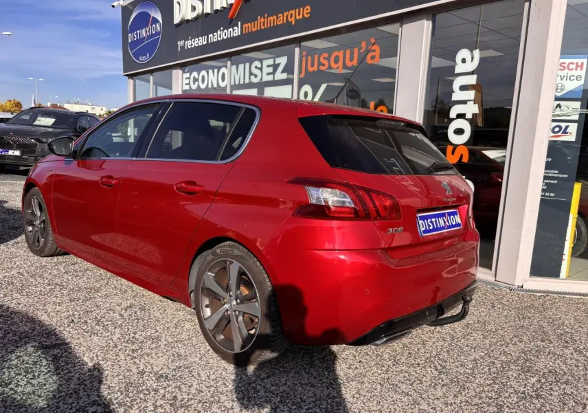 Vue 3/4 arrière droite d'une Peugeot 308 GT Line rouge foncé avec jantes diamantées et toit panoramique stationnée devant un showroom