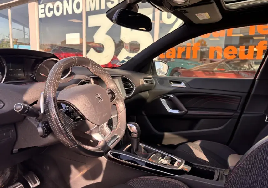 Intérieur avant droit de la Peugeot 308 GT Line 2016 avec volant cuir perforé et surpiqûres rouges visibles.
